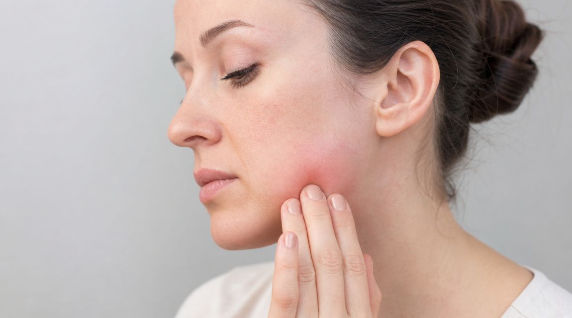 Skotzko Family Dental Clinic | Urgent: Signs of Tooth Infection You Need to Know in 2026 A woman touching her cheek while experiencing pain and swelling indicative of a dental issue.